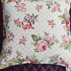 May include: A white pillow with a floral pattern featuring pink, red, and purple roses. The pillow has a white background with small gray polka dots.
