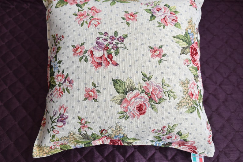 May include: A white pillow with a floral pattern featuring pink, red, and purple roses. The pillow has a white background with small gray polka dots.