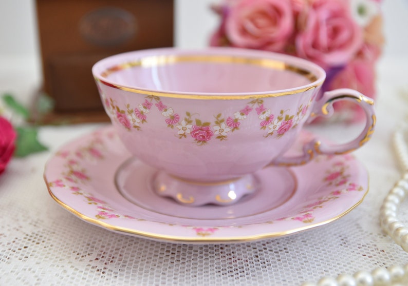 Puede incluir: Un juego de taza y platillo de t&eacute; rosa con un patr&oacute;n floral y ribete dorado. La taza de t&eacute; tiene un asa delicada y el platillo tiene un borde festoneado.