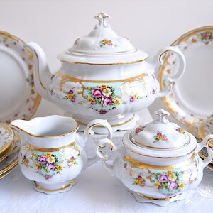May include: A vintage porcelain tea set with floral designs in shades of pink, yellow, and green. The set includes a teapot, sugar bowl, creamer, two teacups, and saucers.