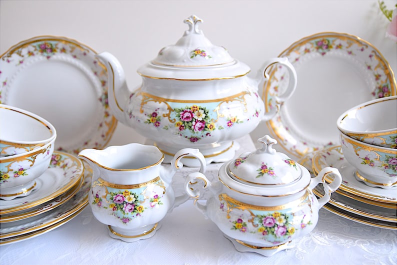 May include: A vintage porcelain tea set with floral designs in shades of pink, yellow, and green. The set includes a teapot, sugar bowl, creamer, two teacups, and saucers.