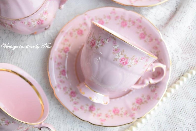 Puede incluir: Un juego de taza y platillo de t&eacute; rosa con un patr&oacute;n floral. La taza de t&eacute; tiene un borde dorado y el platillo tiene un borde festoneado.
