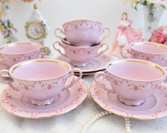 May include: Set of six pink porcelain soup bowls with floral designs and gold trim. Each bowl is paired with a matching saucer.