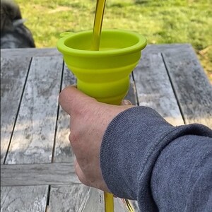 May include: A person pouring yellow liquid from a bottle into a green silicone funnel. The funnel is collapsible and has a wide opening.