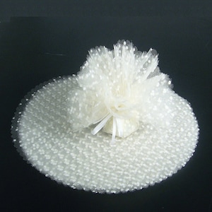 May include: White tulle fabric with small white polka dots. The tulle is gathered into a round shape with a white ribbon tied in a bow.