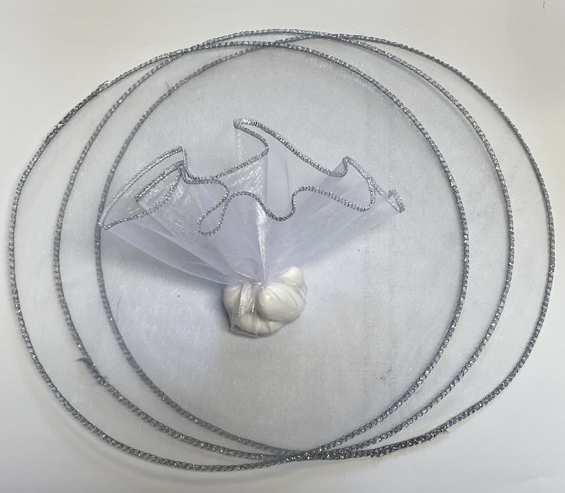 May include: White tulle favor bag with a silver trim, tied with a silver ribbon. The bag is filled with white candy.