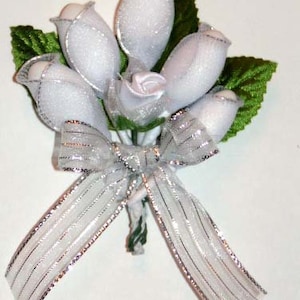 May include: A bouquet of white silk roses tied with a silver ribbon. The roses are arranged in a cluster and tied together with a silver ribbon. The bouquet is perfect for a wedding or other special occasion.
