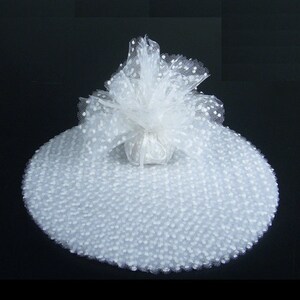 May include: White tulle fabric with small white polka dots. The tulle is gathered into a ball shape and tied with a white ribbon.