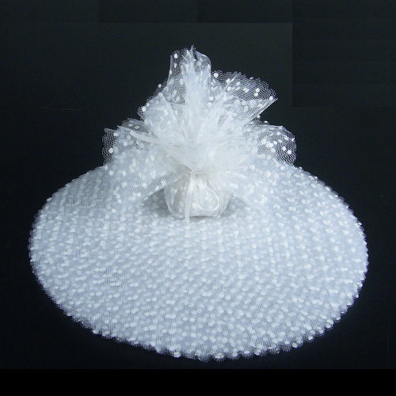 May include: White tulle fabric with small white polka dots. The tulle is gathered into a ball shape and tied with a white ribbon.