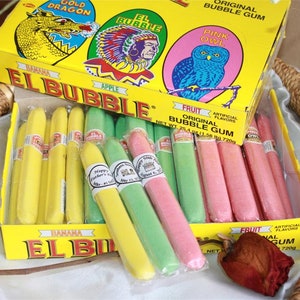 May include: A box of El Bubble Original Bubble Gum in a variety of flavors, including banana, apple, fruit, gold dragon, pink owl. The box is yellow with red and blue accents. The gum is packaged in individual wrappers and is shaped like a cigar. The box is open and the gum is visible inside.