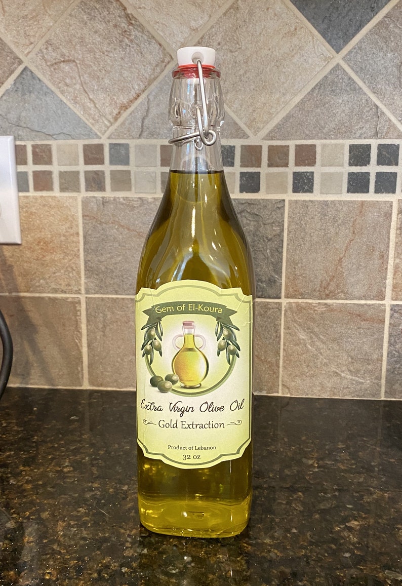 May include: A clear glass bottle of extra virgin olive oil with a green label that reads "Gem of El-Koura Extra Virgin Olive Oil Gold Extraction Product of Lebanon 32 oz".