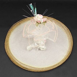 May include: A white tulle veil with a gold trim and a pink flower embellishment. The veil is decorated with a sparkly blue and white fiber optic strand.