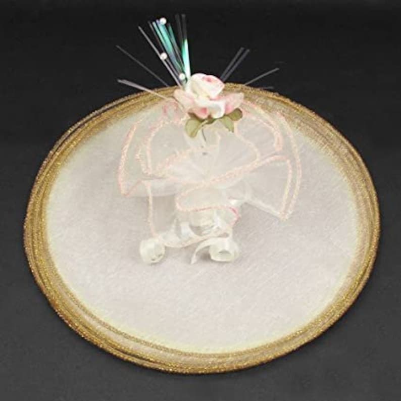 May include: A white tulle veil with a gold trim and a pink flower embellishment. The veil is decorated with a sparkly blue and white fiber optic strand.