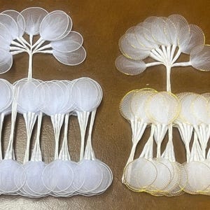 May include: Two sets of white mesh circles with gold wire accents. Each set has 20 circles, with the circles in each set stacked on top of each other. The circles are attached to white stems.