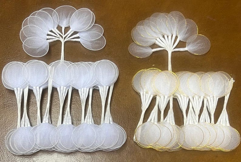 May include: Two sets of white mesh circles with gold wire accents. Each set has 20 circles, with the circles in each set stacked on top of each other. The circles are attached to white stems.