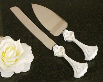May include: White cake server set with a floral design. The server has a silver blade and a white handle with a floral design.