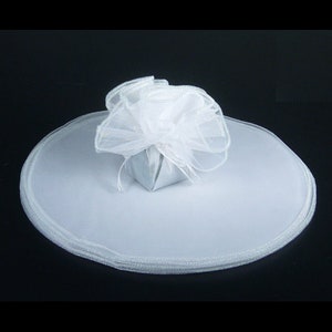 May include: White tulle fabric with a small white gift box in the center. The tulle is gathered around the box and has a white ribbon tied around it.