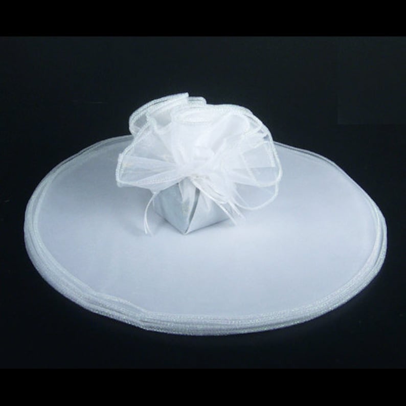 May include: White tulle fabric with a small white gift box in the center. The tulle is gathered around the box and has a white ribbon tied around it.