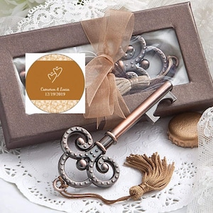 May include: A vintage-style key bottle opener with a gold tassel, packaged in a brown box with a personalized sticker that reads "Cameron & Lucia 12/19/2019".