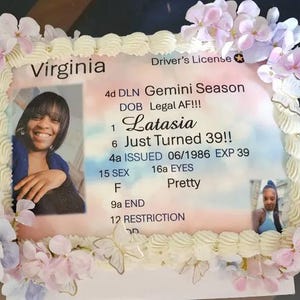 May include: A rectangular cake decorated with white frosting borders and pastel artificial flowers. The top features an edible print of a Virginia driver's license with the name Latasia, text reading Gemini Season, Legal AF, and Just Turned 39.