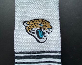 May include: White kitchen towel with black stripes and an embroidered Jacksonville Jaguars logo featuring a teal and gold jaguar head.