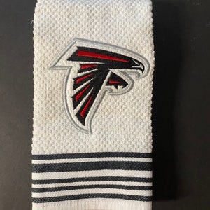Könnte beinhalten: Weißes Küchentuch mit einem gestickten Atlanta Falcons-Logo in Schwarz und Rot. Das Handtuch hat einen schwarz-weißen Streifenrand.