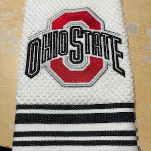 May include: White kitchen towel with black and white stripes. The towel features an embroidered Ohio State logo with a red 'O' and grey outline.
