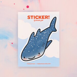 May include: A blue whale shark sticker with white spots. The sticker has a smiling face and is on a white background with clouds. The text "STICKER! bylauren yoo" is at the top of the sticker.