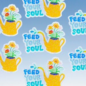 May include: Six colorful stickers with a yellow watering can filled with flowers and the text "Feed Your Soul" in blue and white lettering. The stickers have a glittery finish.