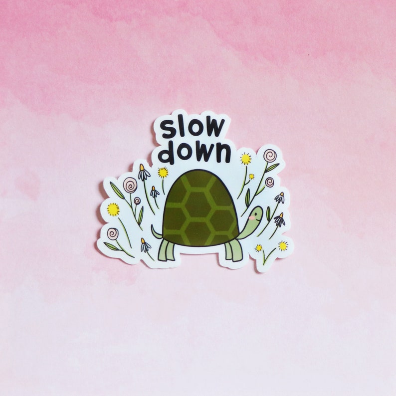 Op de afbeelding: Een sticker met een groene schildpad die door een veld met bloemen loopt. De tekst "slow down" staat boven de schildpad.