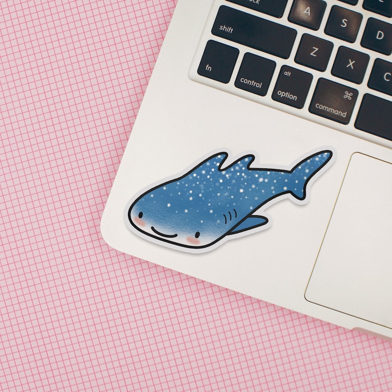 May include: A blue and white whale shark sticker with a smiling face. The sticker is on a white laptop.