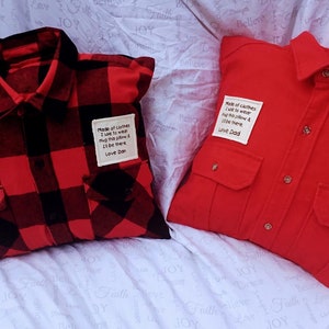 May include: Two red and black plaid and red pillow covers made from shirts. The pillows have a white label sewn on them that says "Made of clothes I use to wear hug this pillow & I'll be there Love Dad" and "Made of clothes I use to wear hug this pillow & I'll be there Love Dan".