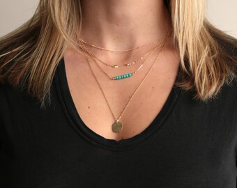 May include: A layered gold necklace with a turquoise bead bar and a round pendant.