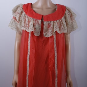 May include: A long, coral-colored nightgown with a lace trim around the neckline and sleeves. The gown has a sheer, lightweight fabric.