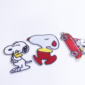 Puede incluir: Tres parches bordados para planchar con el personaje de dibujos animados Snoopy. Un parche muestra a Snoopy conduciendo un coche rojo descapotable, otro muestra a Snoopy durmiendo y el tercero muestra a Snoopy sosteniendo un objeto amarillo.