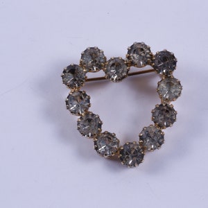 May include: A gold heart-shaped brooch with clear rhinestones.