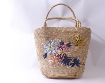 May include: A straw tote bag with a woven texture and embroidered floral design in shades of blue, pink, yellow, and green.