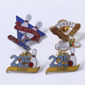 May include: Four enamel pins with bowling themes. One pin features a red, white, and blue design with the text "PINS OVER GAME" and "USBC." Another pin depicts a golden eagle with "SNBA" and "HIGH SERIES." Two pins display "225 GAME."