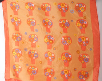 May include: Orange square scarf with a repeating pattern of stylized flower bouquets in orange, yellow, blue, and white. The scarf has a solid orange border and is hanging against a white background.