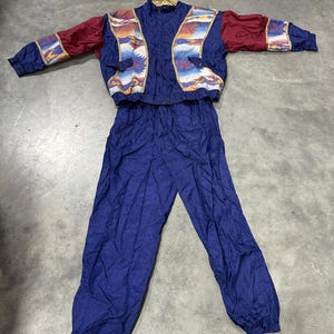 May include: A vintage two-piece tracksuit set. The jacket is navy blue with burgundy sleeves and a colorful geometric pattern across the shoulders and chest. The matching pants are navy blue. The set is made of a lightweight, possibly nylon, material.