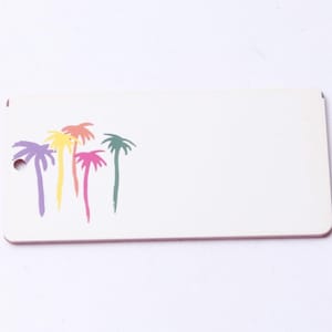 May include: A rectangular white tag with a hole in the upper left corner. The tag features a colorful palm tree design in purple, yellow, orange, pink, and green. The tag has a pink border.