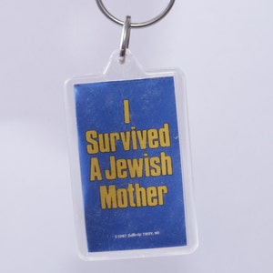 以下が含まれることがあります： 「I Survived A Jewish Mother」と書かれた青と黄色のキーホルダーです。