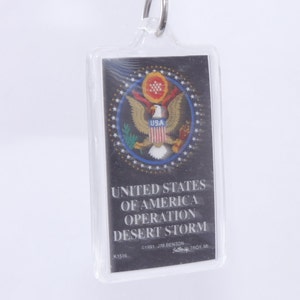 May include: A clear plastic keychain with a black and white image of the Great Seal of the United States. The text "UNITED STATES OF AMERICA OPERATION DESERT STORM" is printed below the image.