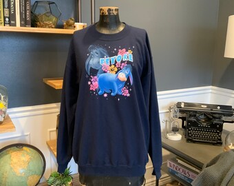 May include: A navy blue sweatshirt with a graphic of Eeyore from Winnie the Pooh. The graphic features Eeyore with flowers and the text "Eeyore" in pink and blue.