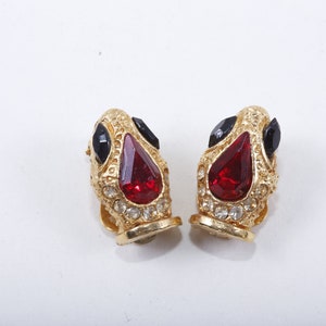 Puede incluir: Un par de pendientes de clip de tono dorado con piedras rojas y negras. Los pendientes tienen forma de lágrima y un diseño detallado.