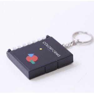 May include: Black keychain with the text "COLORFORMS" and a colourful geometric design. The design includes a red circle, a blue triangle, and a green rectangle. The keychain has a silver ring.