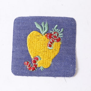 May include: A blue denim patch with an embroidered yellow heart-shaped apple with two red worms on it.