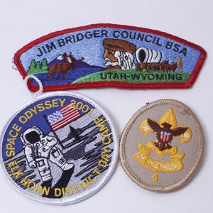 May include: Three embroidered patches, one with a blue background and the text "Jim Bridger Council BSA Utah-Wyoming", one with a blue and white background and the text "Space Odyssey 2007 Elk Horn District Day Camp", and one with a tan background and the text "Be Prepared" with a golden eagle and fleur-de-lis.