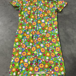 May include: A vintage, short-sleeved dress with a vibrant floral pattern. The dress features a green background with large, colorful flowers in shades of yellow, orange, pink, and blue. It has a collared neckline and a full-length zipper down the front.