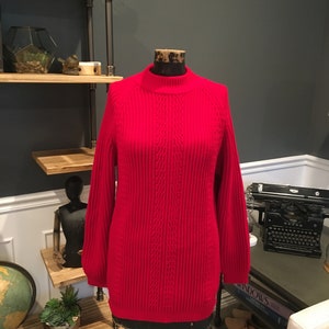 Puede incluir: Suéter de punto rojo con cuello alto y mangas largas. El suéter está en un maniquí.